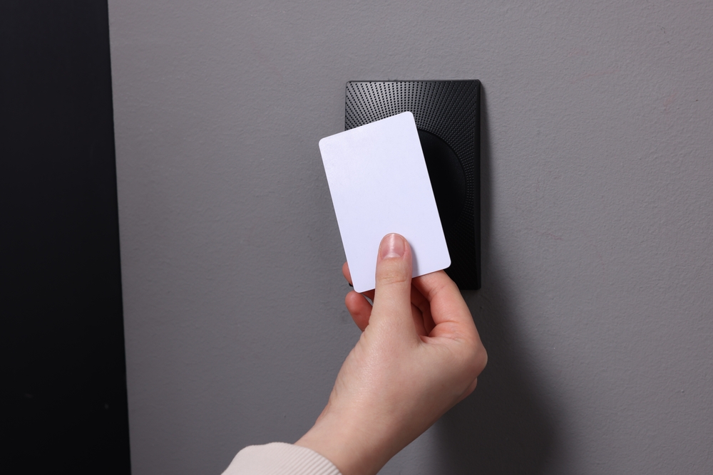 person holing up access control key to reader on a gray wall